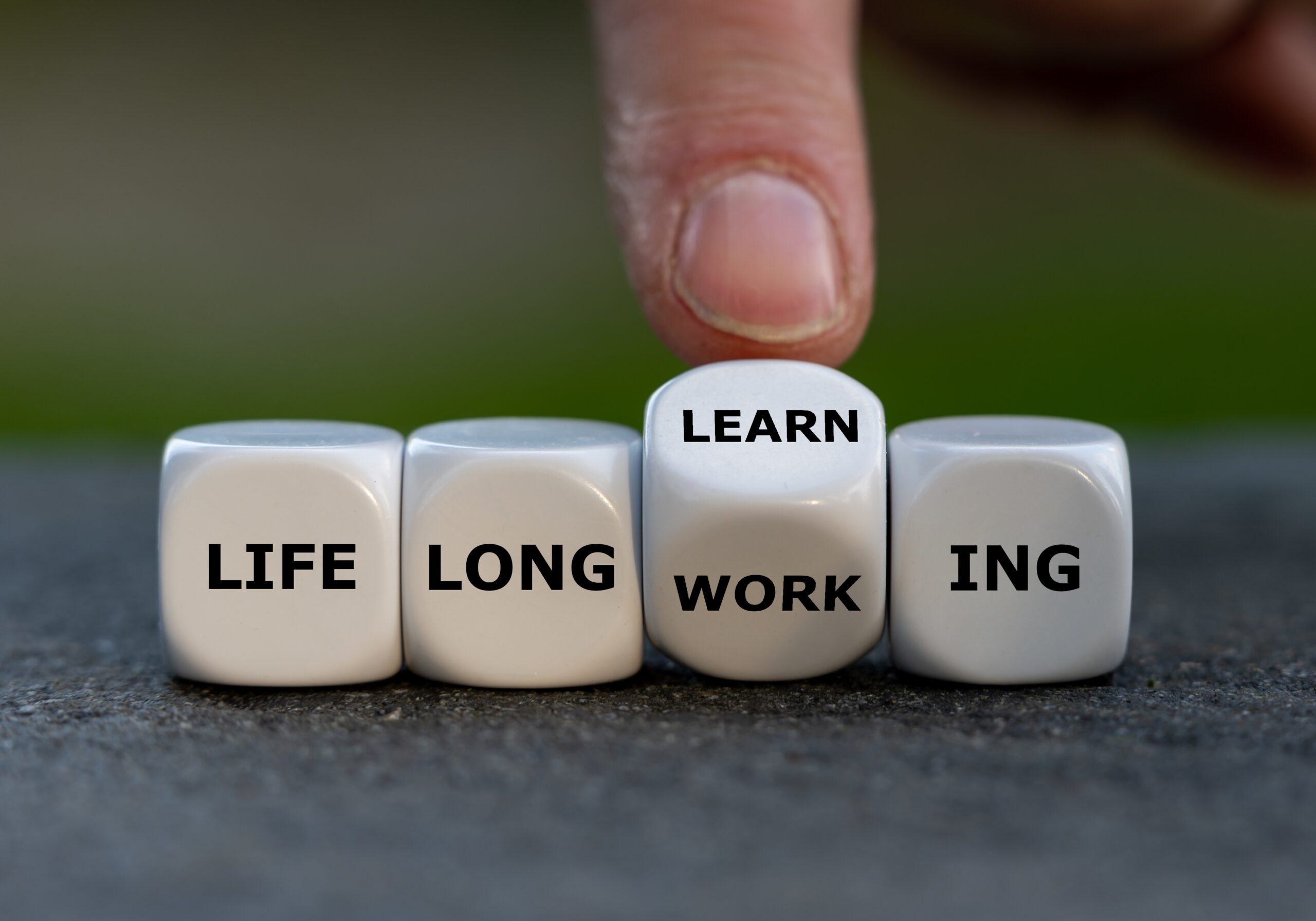 hand turns dice and changes the expression 'life long working' to ' life long learning'. shutterstock 2239946565